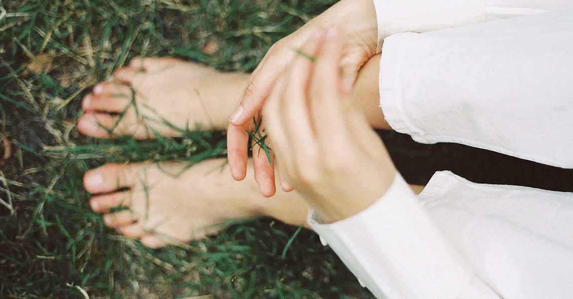 Bare feet in the grass with hands resting nearby, grounded and present